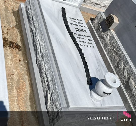מצבה מאבן עם כיתוב בעברית ואבנים שחורות